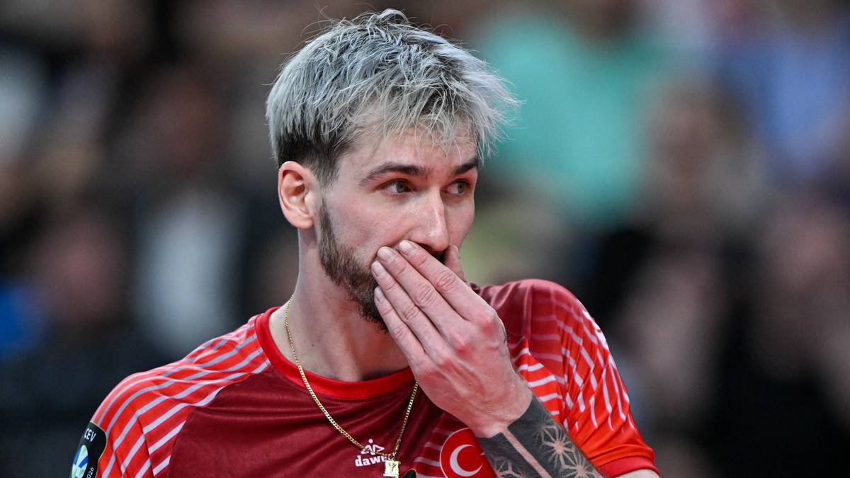 Mężczyzna w czerwonej koszulce sportowej, zasłaniający usta dłonią.