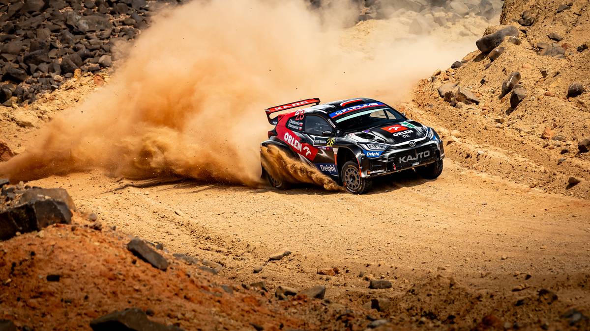 Samochód rajdowy ORLEN Rally Team wjeżdża w zakręt, wzbijając dużą chmurę kurzu.