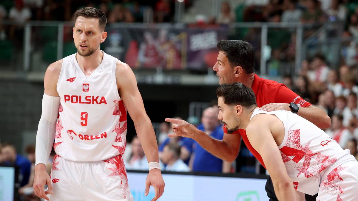 Dwóch zawodników drużyny koszykarskiej w białych koszulkach z numerami i logo Polski podczas meczu. Jeden zawodnik ma numer 9 na koszulce.