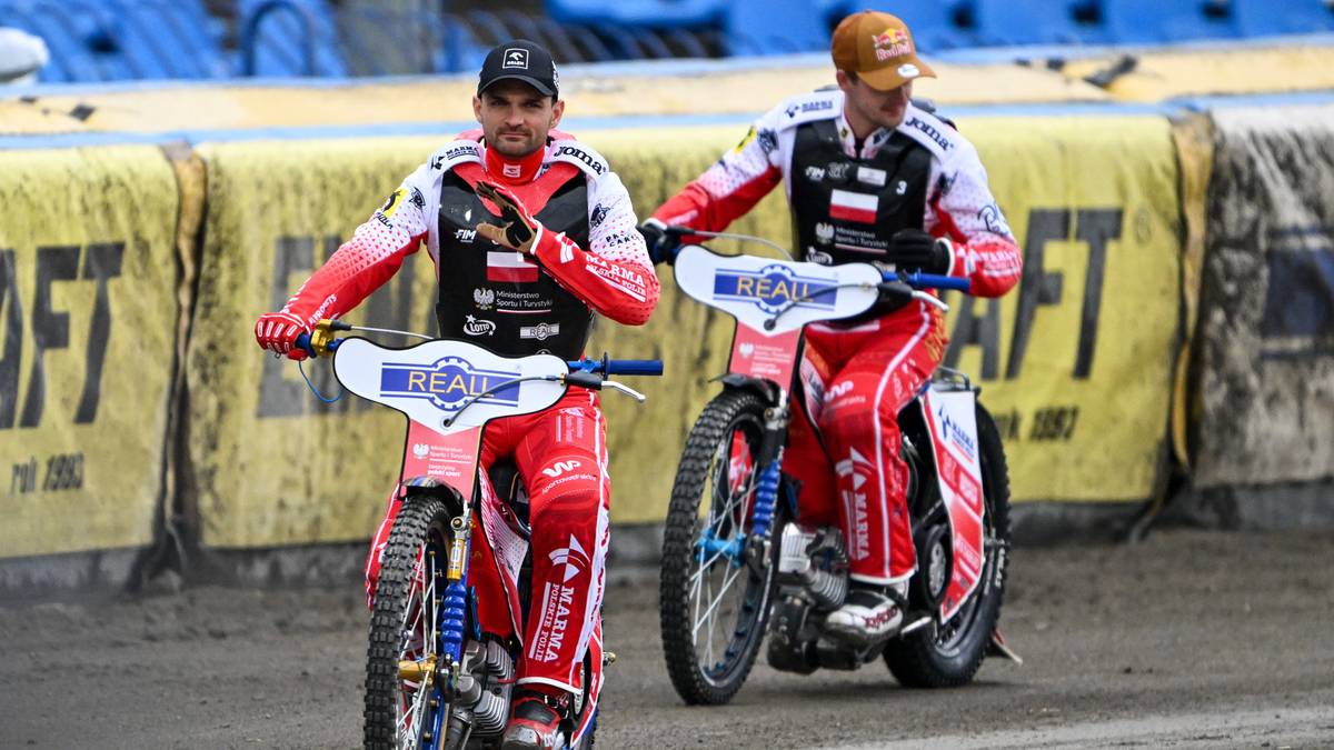 Dw&oacute;ch żużlowc&oacute;w w czerwonych kombinezonach siedzi na motocyklach.