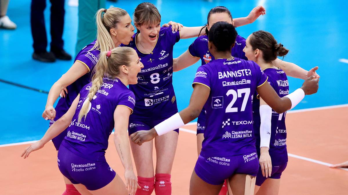 Siatkarki w fioletowych strojach świętują zwycięstwo, przytulając się na boisku.