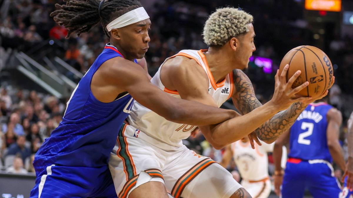 Dwóch graczy NBA podczas meczu, jeden w białym stroju z pomarańczowymi pasami trzyma piłkę i jest broniony przez gracza w niebieskim stroju.