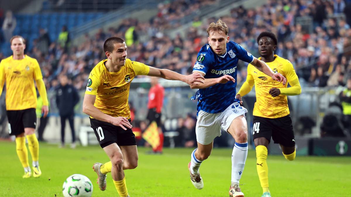 Piłkarze w ż&oacute;łtych i niebieskich strojach rywalizują o piłkę na boisku piłkarskim.