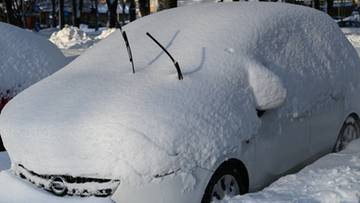 Samoch&oacute;d całkowicie pokryty grubą warstwą śniegu, z widocznymi wycieraczkami sterczącymi ze śniegu.