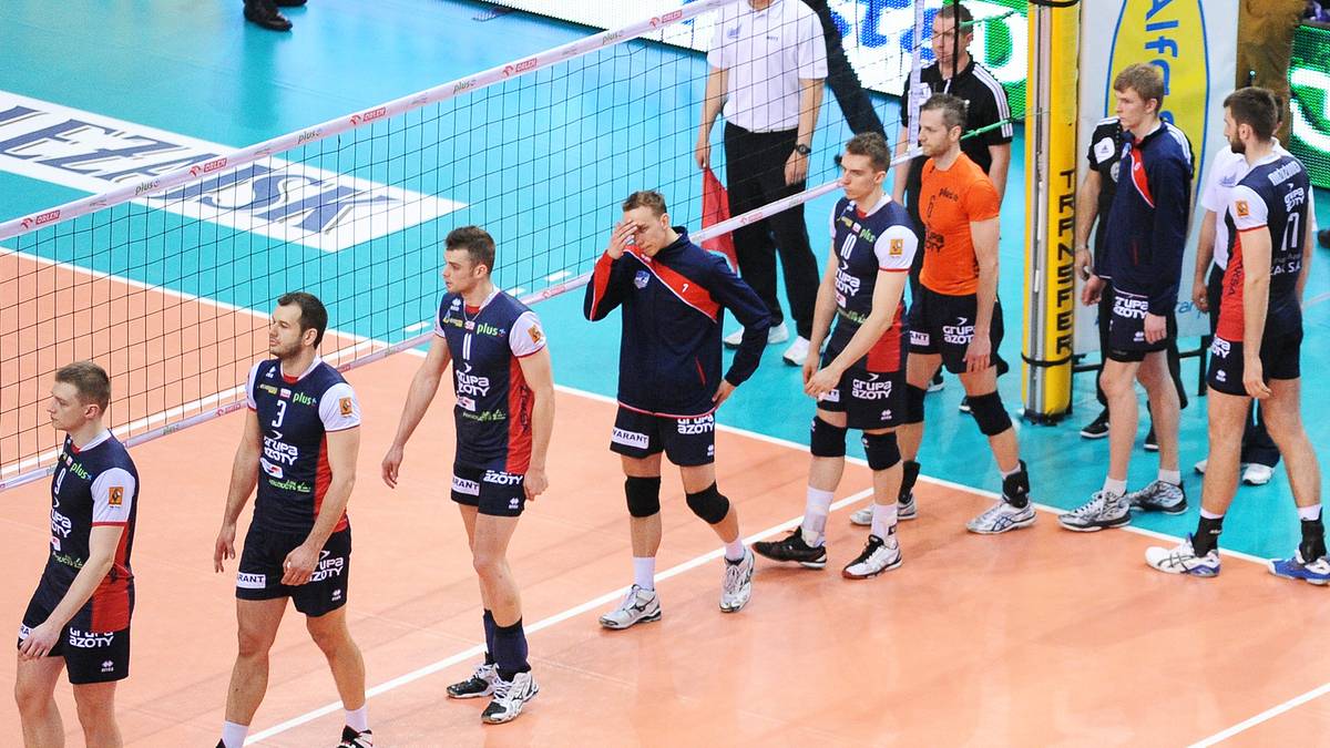 Siatkarze w strojach sportowych stoją na boisku siatkarskim.