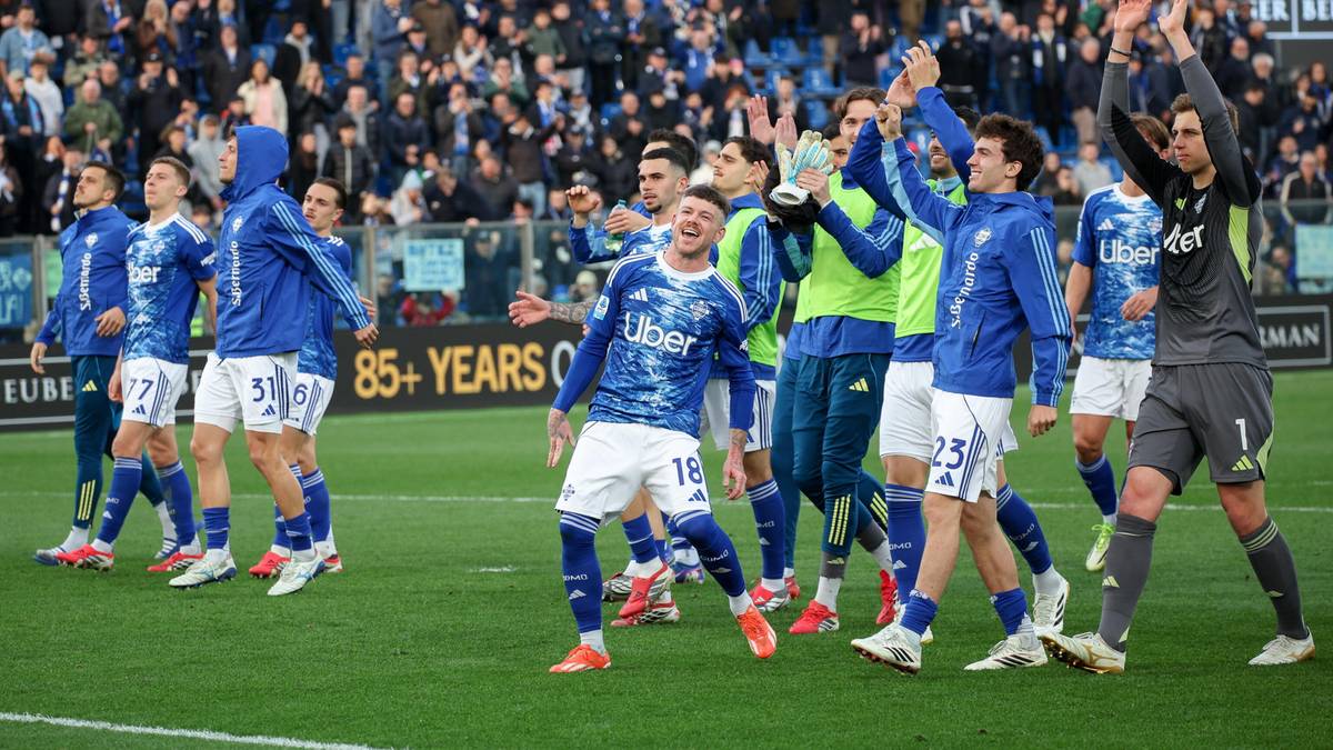 Grupa piłkarzy w niebiesko-białych strojach świętuje na boisku, podnosząc ręce w geście radości.