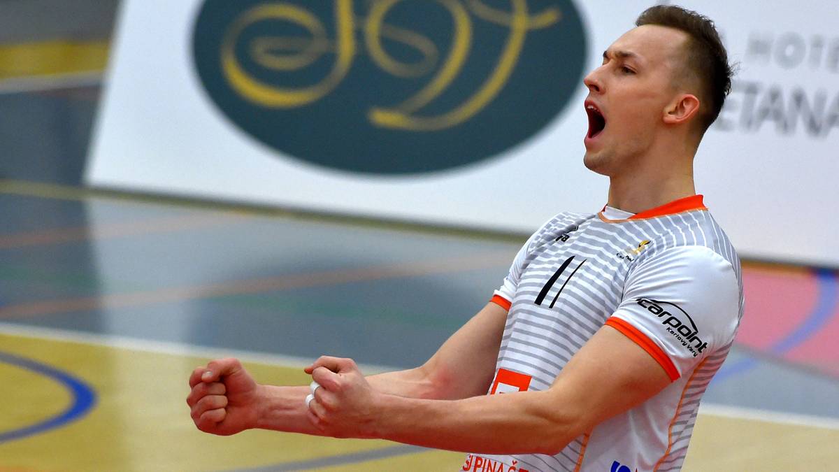 Siatkarz w białej koszulce z białymi i szarymi pasami, z pomarańczowymi wstawkami, krzyczy z zaciśniętymi pięściami.