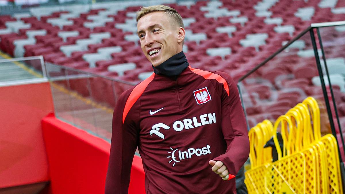 Młody piłkarz w bordowej koszulce z logo Orlen, uśmiecha się podczas pobytu na stadionie.