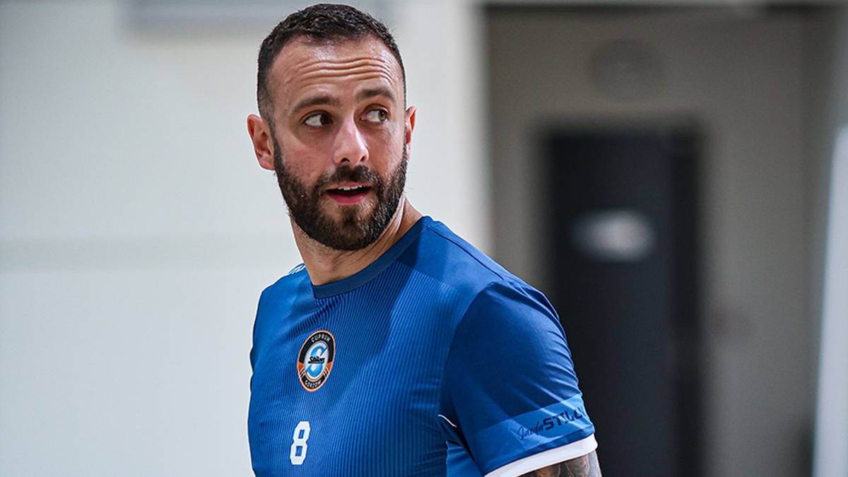 Portret mężczyzny z krótką czarną brodą, ubranego w niebieską koszulkę z numerem 8 i białymi rękawami.