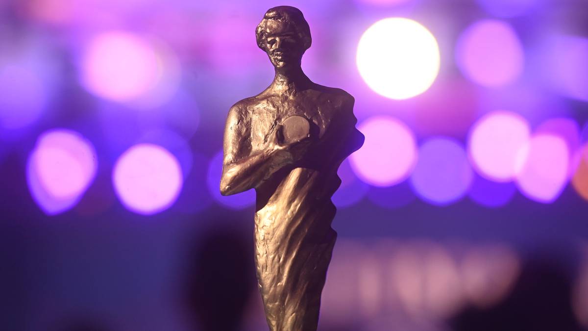 Statuetka nagrody w kształcie ludzkiej postaci na rozmytym fioletowo-r&oacute;żowym tle z okręgami światła.