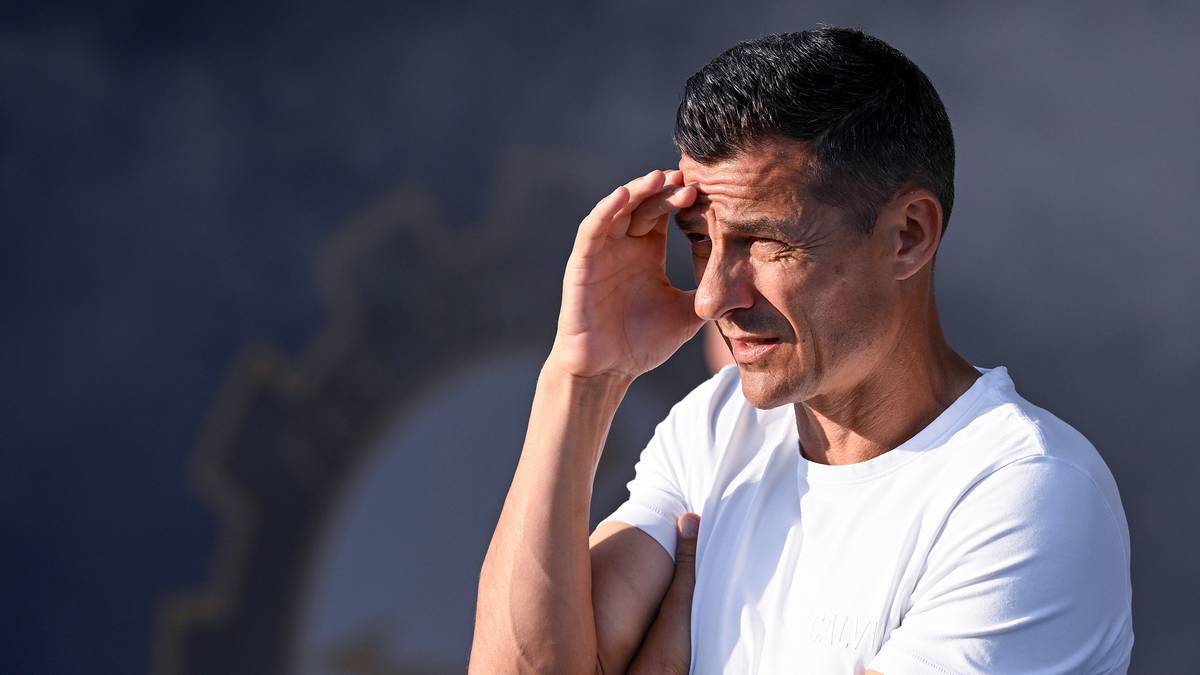 Mężczyzna w białej koszulce trzyma się za czoło, wyrażając zmartwienie lub stres.