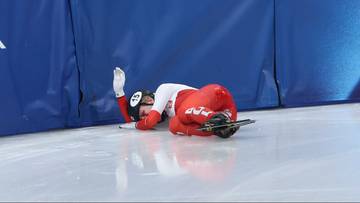 Zawodniczka short tracku w czerwonym stroju leży na lodzie po upadku.
