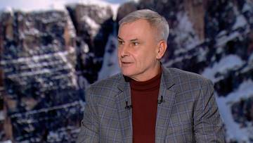 Portret mężczyzny w średnim wieku, z siwymi włosami, ubranego w marynarkę w kratę i bordowy golf. W tle widoczny jest zamazany krajobraz g&oacute;rski.