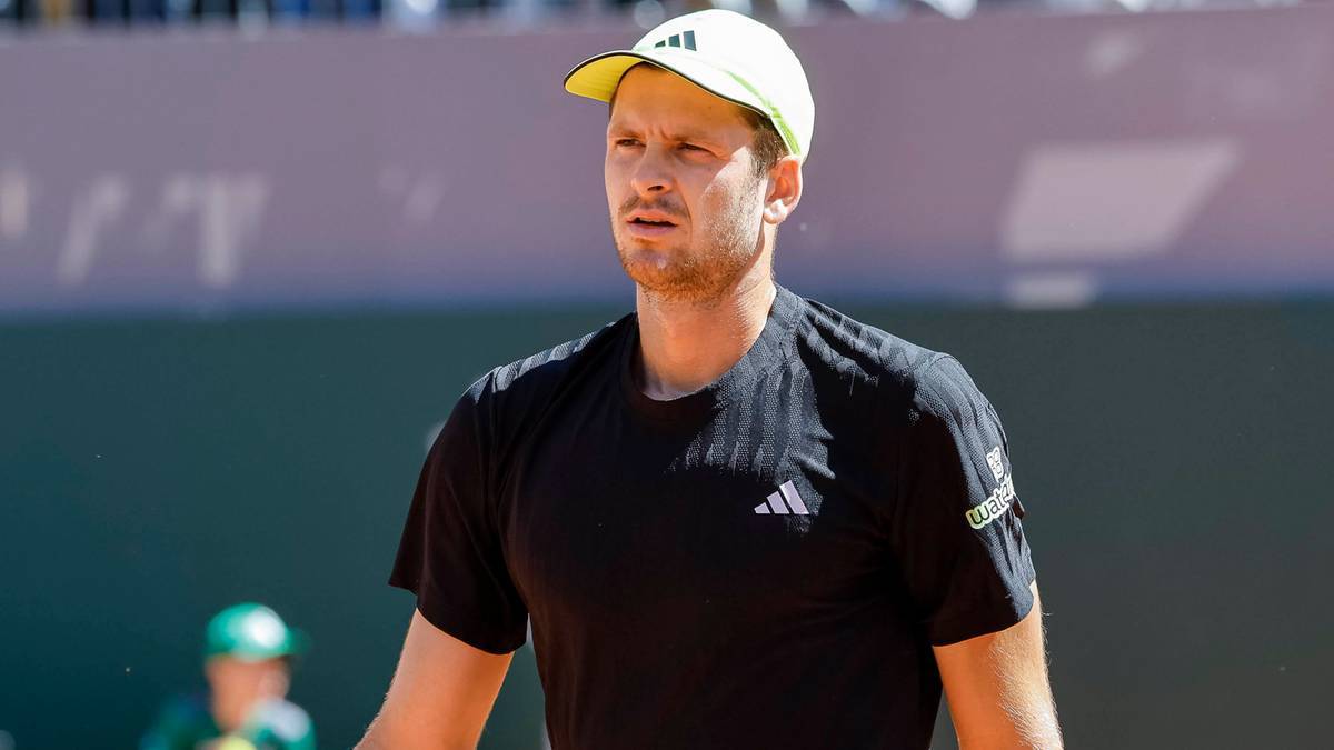 Hubert Hurkacz w czarnym stroju tenisowym i ż&oacute;łtej czapce z daszkiem patrzy przed siebie.