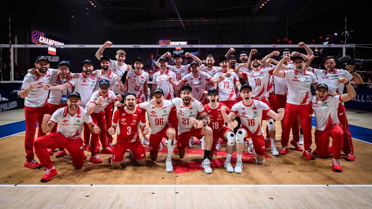 Drużyna męska Polski w siatk&oacute;wce w komplecie pozuje do zdjęcia, stojąc i klęcząc na boisku siatkarskim.