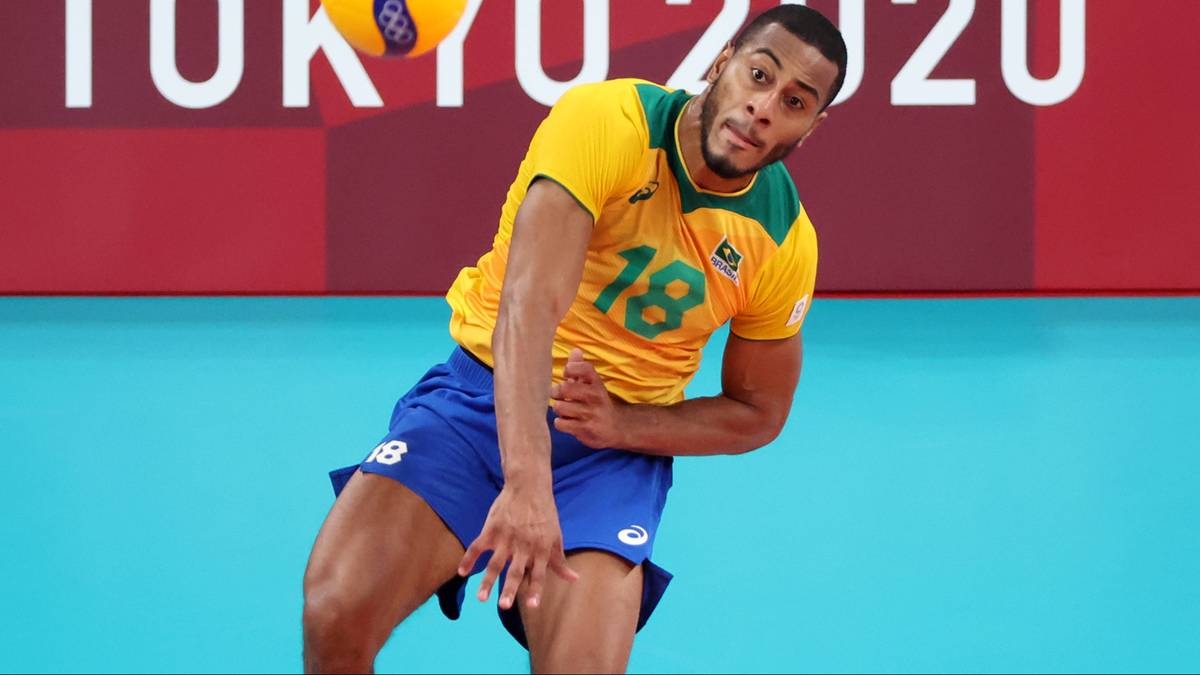 Siatkarz w ż&oacute;łtej koszulce z numerem 18 i niebieskich spodenkach wykonuje zagrywkę z piłką w powietrzu. W tle widnieje napis TOKYO 2020.