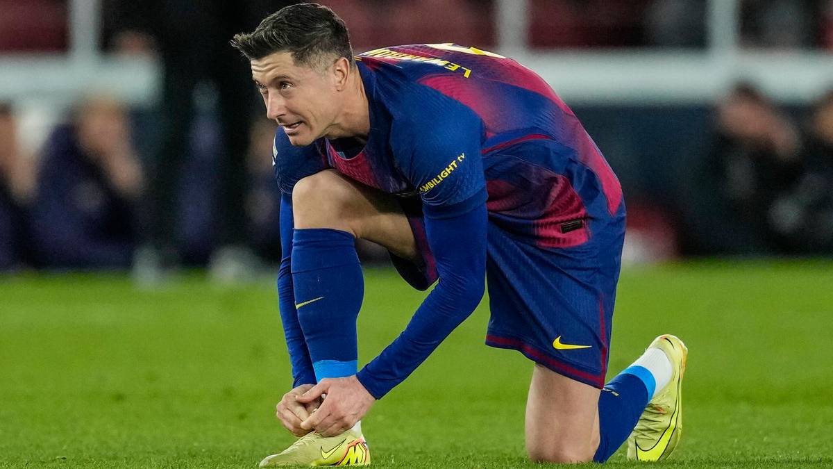Piłkarz FC Barcelony Robert Lewandowski klęczy na boisku, zawiązując sznur&oacute;wki.