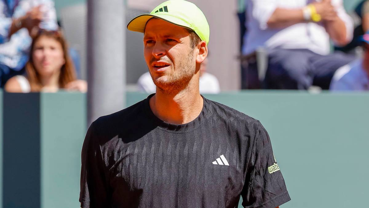 Hubert Hurkacz w czarnej koszulce polo i żółtej czapce z daszkiem na korcie tenisowym.