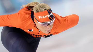 Zawodniczka w pomarańczowym stroju z opaską na głowie z napisem "TeamNL" jedzie na łyżwach