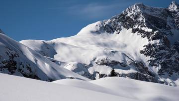 Ośnieżone szczyty g&oacute;rskie w słoneczny dzień z błękitnym niebem.
