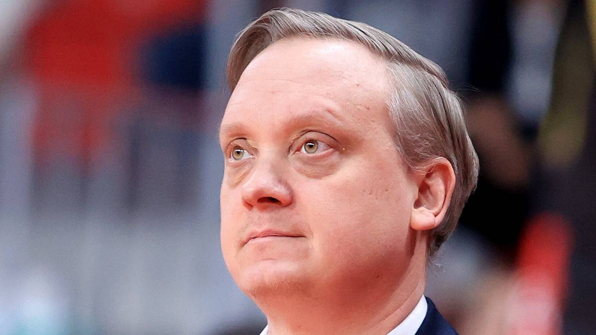 Portret mężczyzny patrzącego w bok, ubranego w białą koszulę i marynarkę.