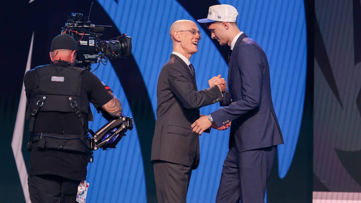 Dwóch mężczyzn w garniturach ściska sobie dłonie na scenie podczas draftu NBA.