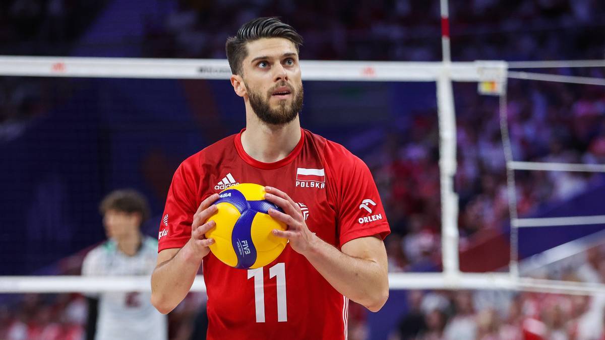 Siatkarz w czerwonej koszulce z numerem 11 na piersi, trzymający piłkę do siatkówki.