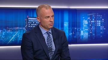 Mężczyzna w garniturze i krawacie siedzi w studiu telewizyjnym.