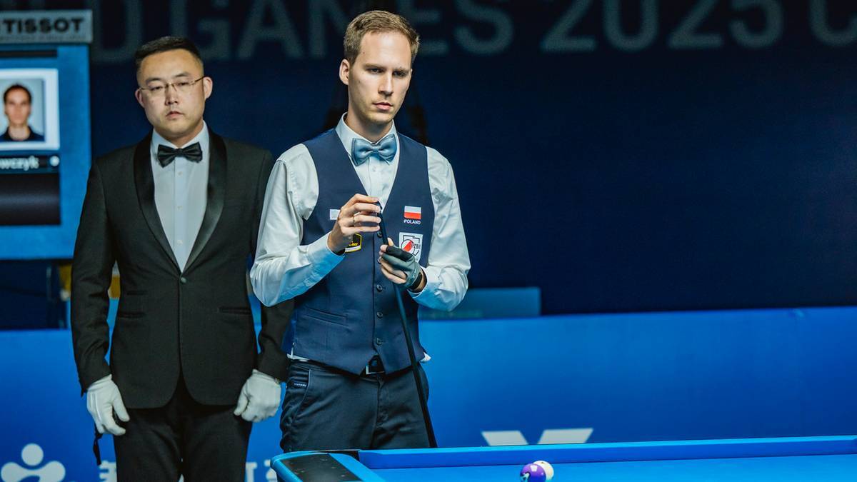 Dwóch mężczyzn w eleganckich strojach stoi obok stołu bilardowego, jeden z nich trzyma telefon w dłoni.