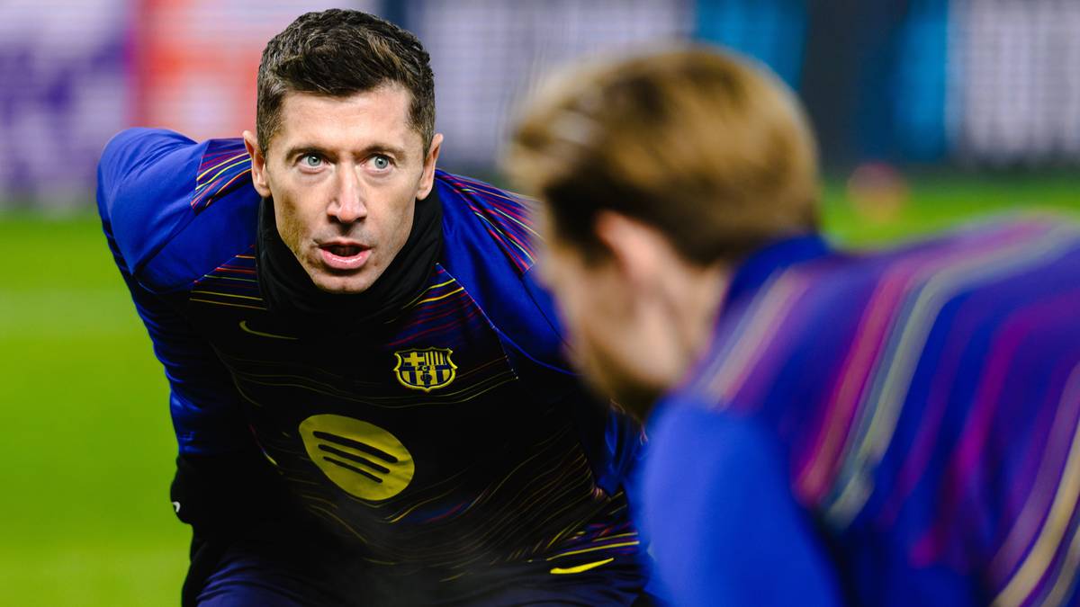 Piłkarz Robert Lewandowski w niebieskiej koszulce FC Barcelony na boisku piłkarskim, patrzący w kierunku innego zawodnika.