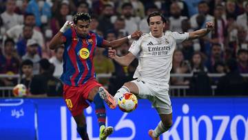 Dw&oacute;ch piłkarzy FC Barcelony i Realu Madryt walczą o piłkę na boisku podczas meczu.