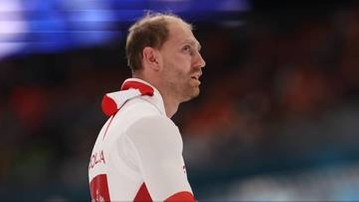 Portret Damiana Żurka, polskiego panczenisty, w białej kurtce sportowej z czerwonymi akcentami.