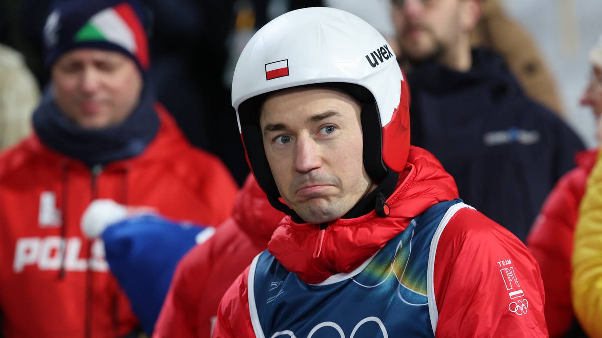 Skoczek narciarski w białym kasku z biało-czerwoną flagą Polski, ubrany w kombinezon z logo Igrzysk Olimpijskich.