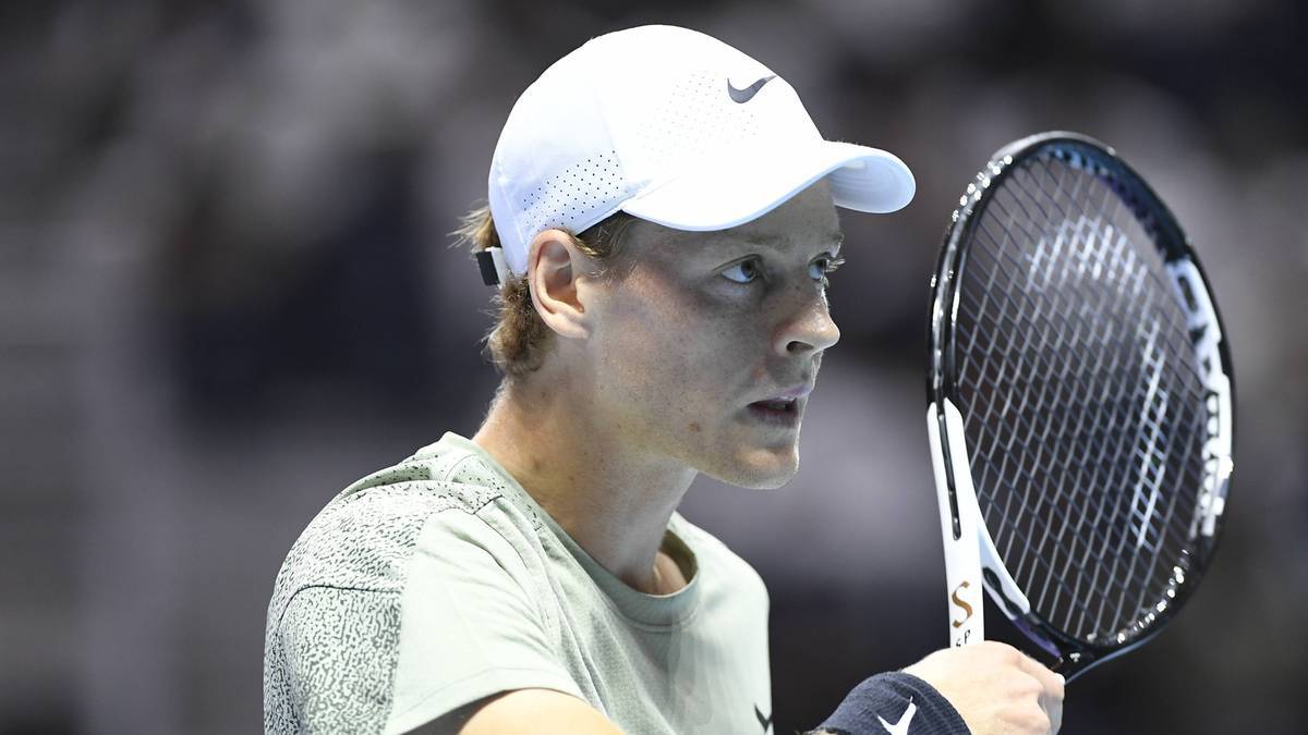 Mężczyzna w białej czapce z daszkiem i zielonej koszulce trzyma rakietę tenisową.