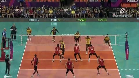 Siatkarze w akcji podczas meczu, jeden z zawodnik&oacute;w wykonuje zagrywkę, pozostali gracze są na boisku, gotowi do odbicia piłki.