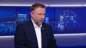 Mężczyzna w garniturze i białej koszuli mówi, na tle ekranów z widokiem nocnego miasta.