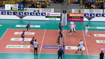 Siatkarze w akcji podczas meczu, jeden z graczy wykonuje blok na siatce, inni zawodnicy są w trakcie gry.