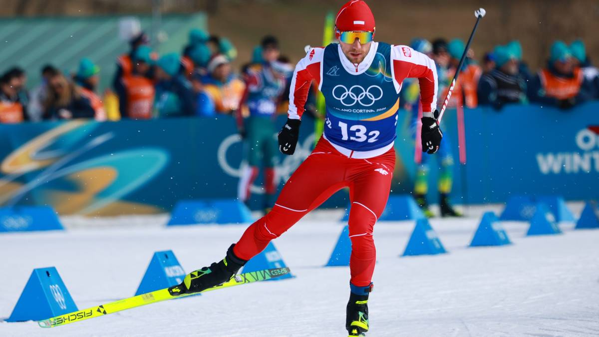 Narciarz biegowy w czerwonym stroju z numerem startowym 132 i symbolem olimpijskim, podczas zawod&oacute;w.