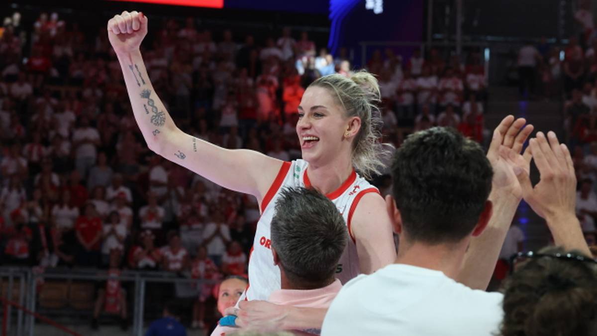 Siatkarka z podniesioną zaciśniętą pięścią w geście triumfu, uśmiechnięta, na tle tłumu kibiców.