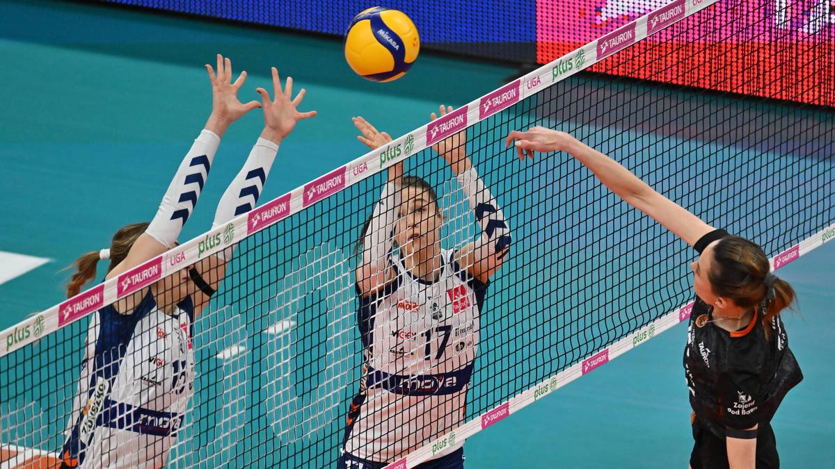 Siatkarki podczas meczu pr&oacute;bują zablokować atak przeciwniczki nad siatką.