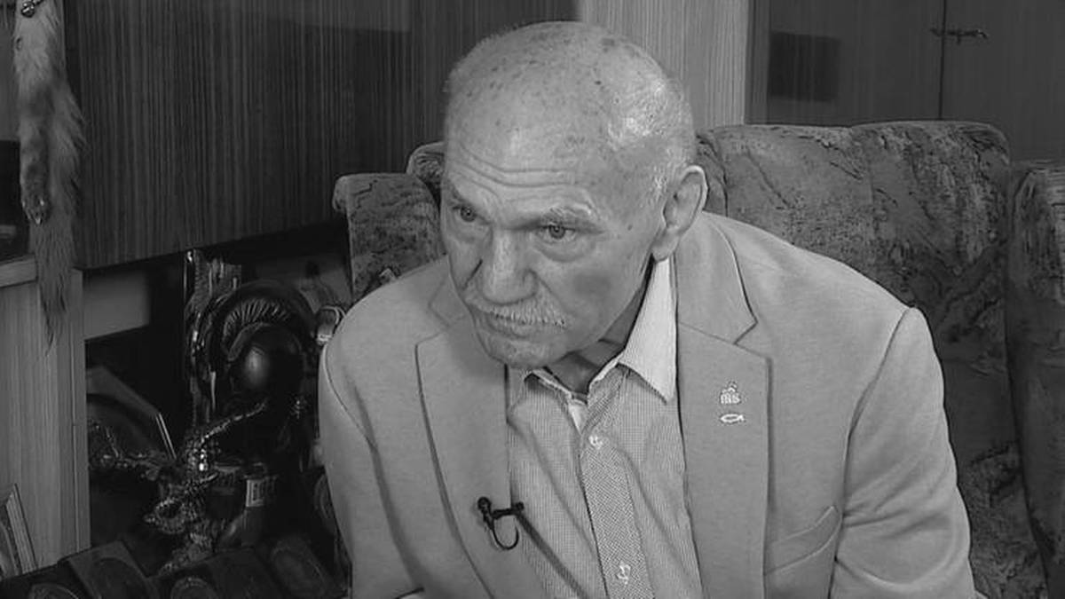 Portret starszego mężczyzny w jasnym garniturze, siedzącego na kanapie w pomieszczeniu.