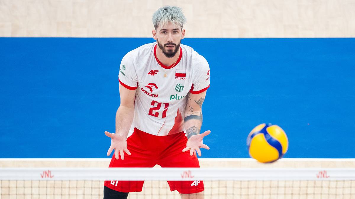 Siatkarz Tomasz Fornal w białej koszulce z numerem 27 i czerwonych spodenkach, patrzy w kierunku piłki do siatkówki lecącej w jego stronę. Dłonie ma otwarte i lekko uniesione, przygotowany do odbioru.