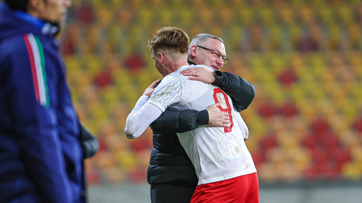 Dw&oacute;ch mężczyzn obejmuje się na boisku piłkarskim, jeden w białej koszulce z numerem 9.
