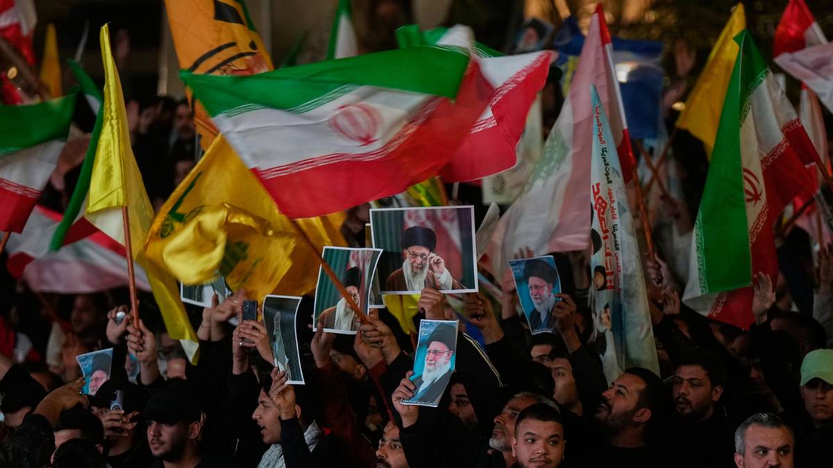 Zgromadzenie ludzi trzymających flagi Iranu i zdjęcia przywódców.