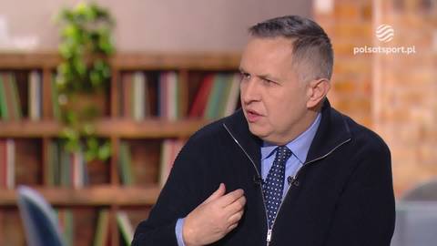 Roman Kosecki w wywiadzie, ubrany w sweter, koszulę i krawat, gestykuluje prawą ręką.