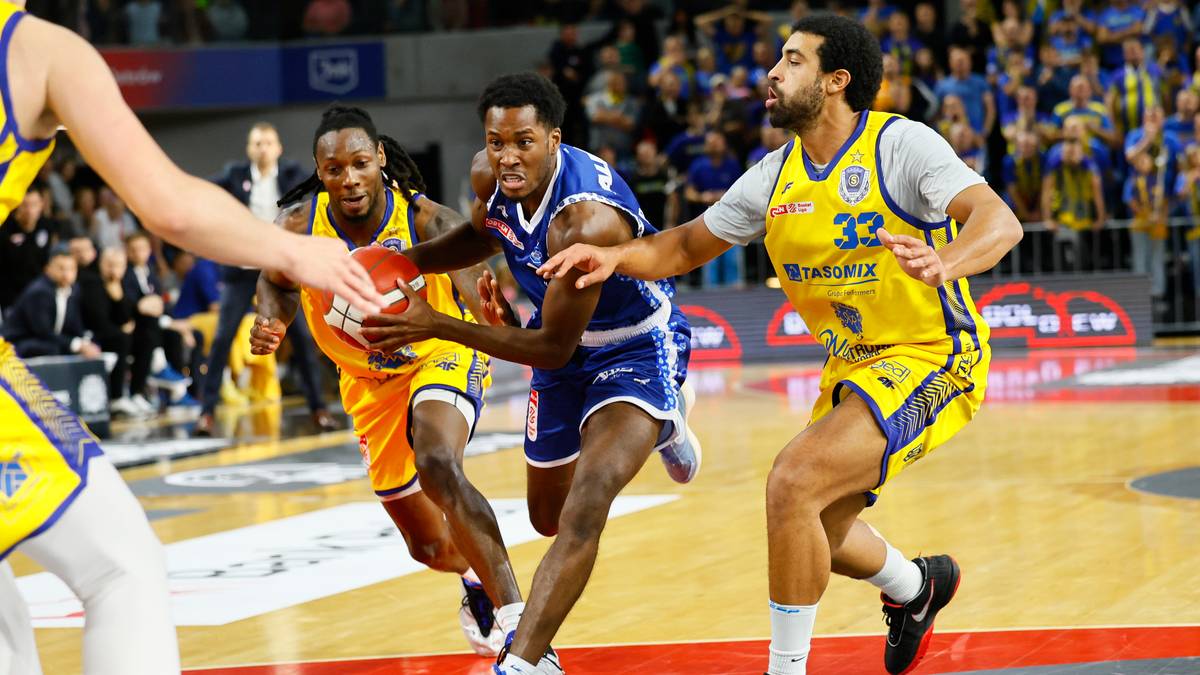 Gracze drużyny w żółtych koszulkach i niebieskich zmagają się w meczu koszykówki. Jeden z graczy w żółtej koszulce z numerem 33 próbuje odebrać piłkę.