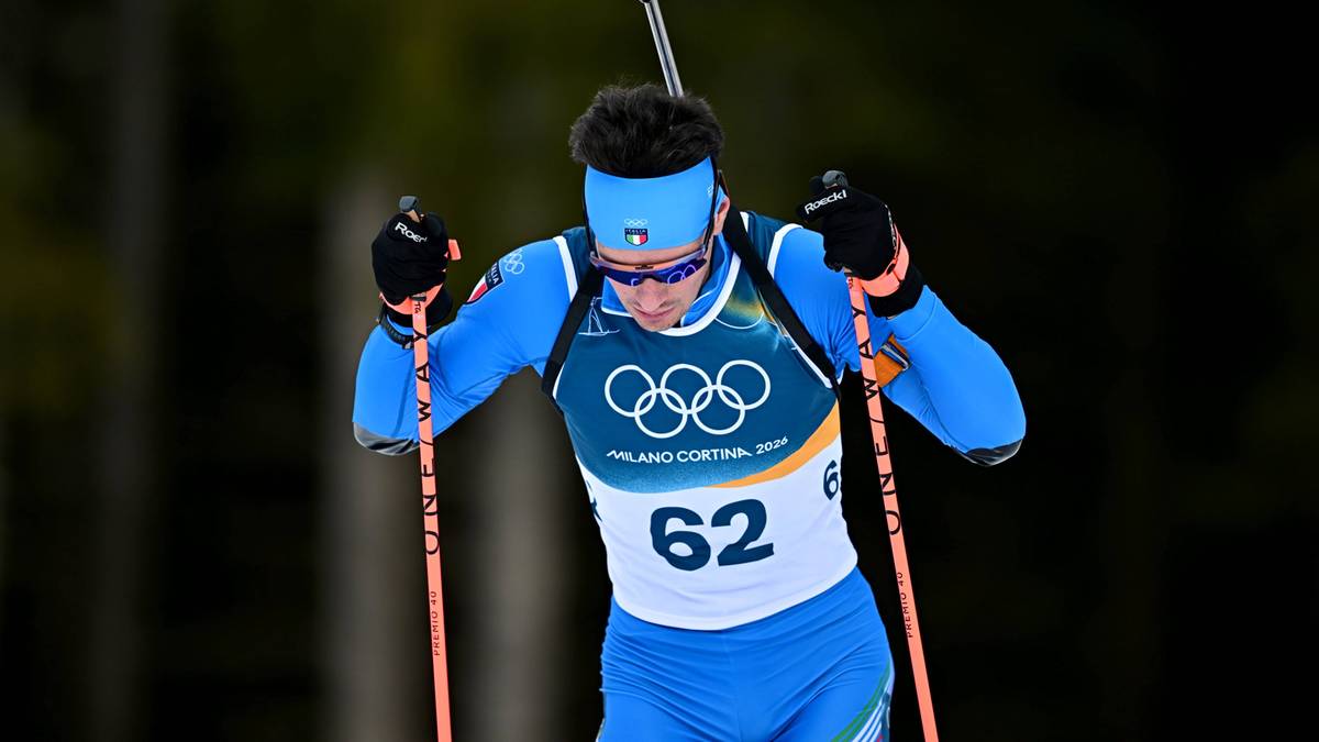 Biathlonista w niebieskim stroju sportowym z numerem 62 na piersi i nartami na nogach, z kijkami w dłoniach, podczas biegu.