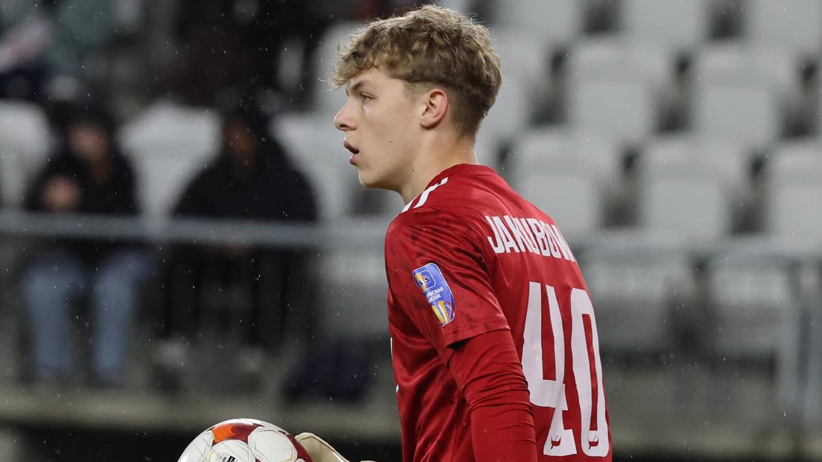 Młody bramkarz w czerwonej koszulce z numerem 40 i białymi rękawicami trzyma piłkę.