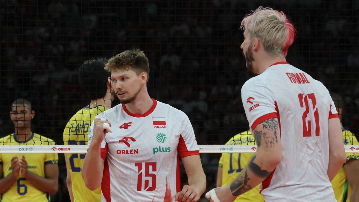 Dwóch siatkarzy w biało-czerwonych strojach świętuje, jeden z nich zaciska pięść. W tle widać innych zawodników i trybuny.