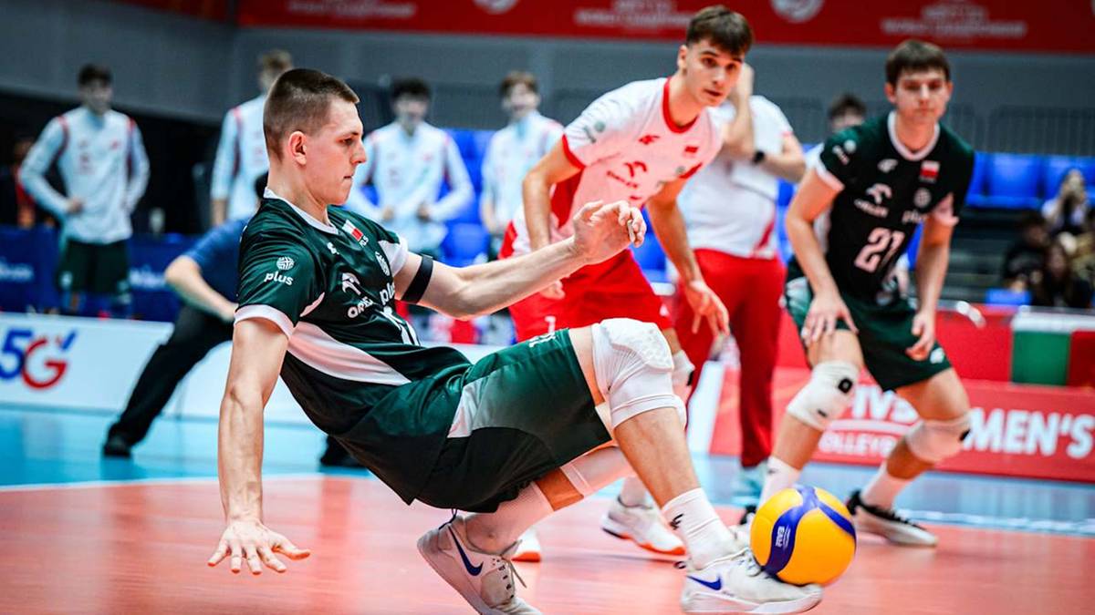 Siatkarz w zielonym stroju pr&oacute;buje obronić piłkę nogą na boisku do siatk&oacute;wki podczas meczu.